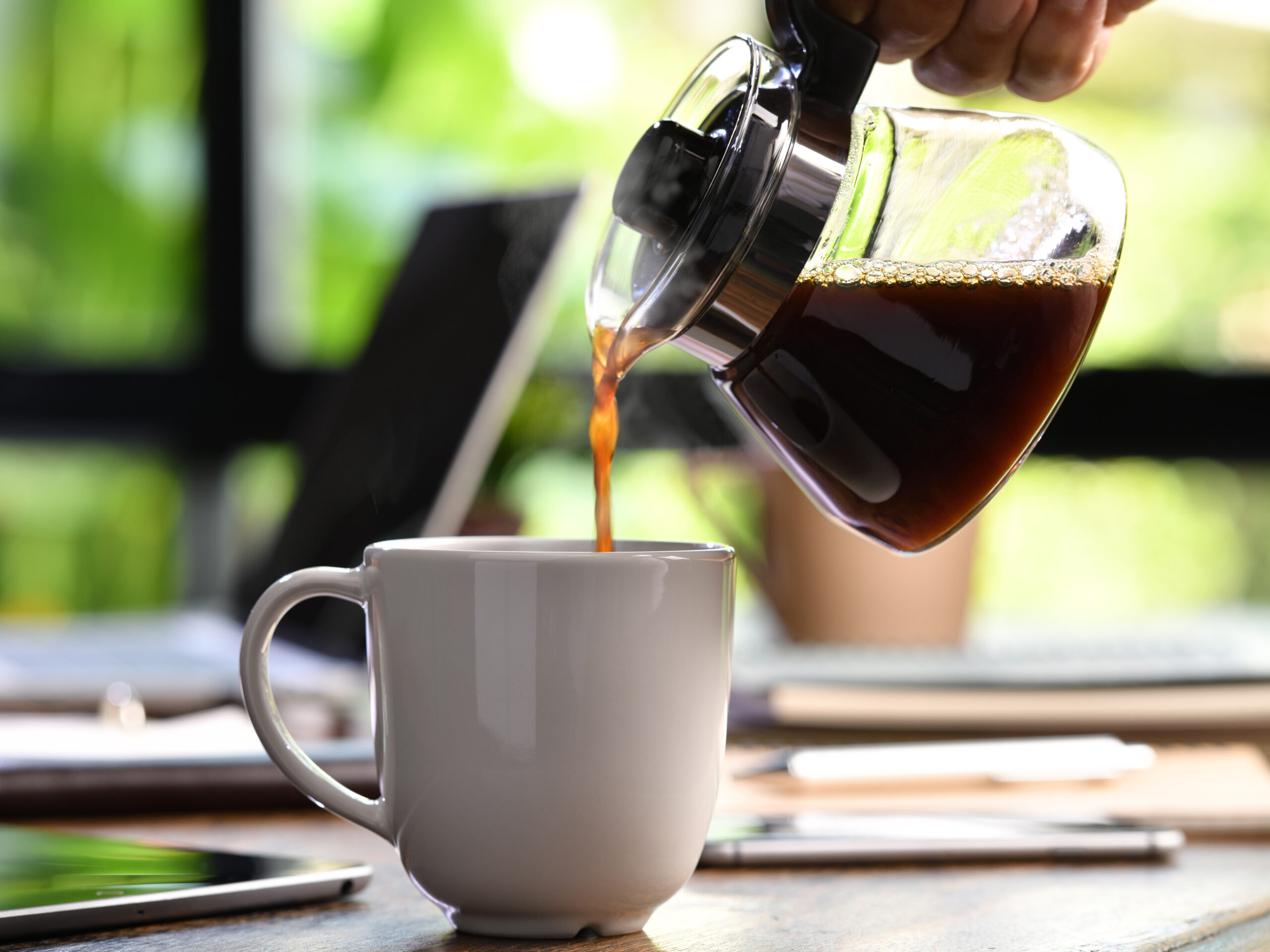 A hand pouring steaming coffee in to a cup on a work desk when work from home