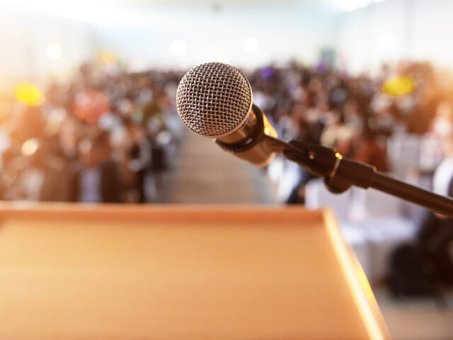 looking over podium at out of focus audience with microphone